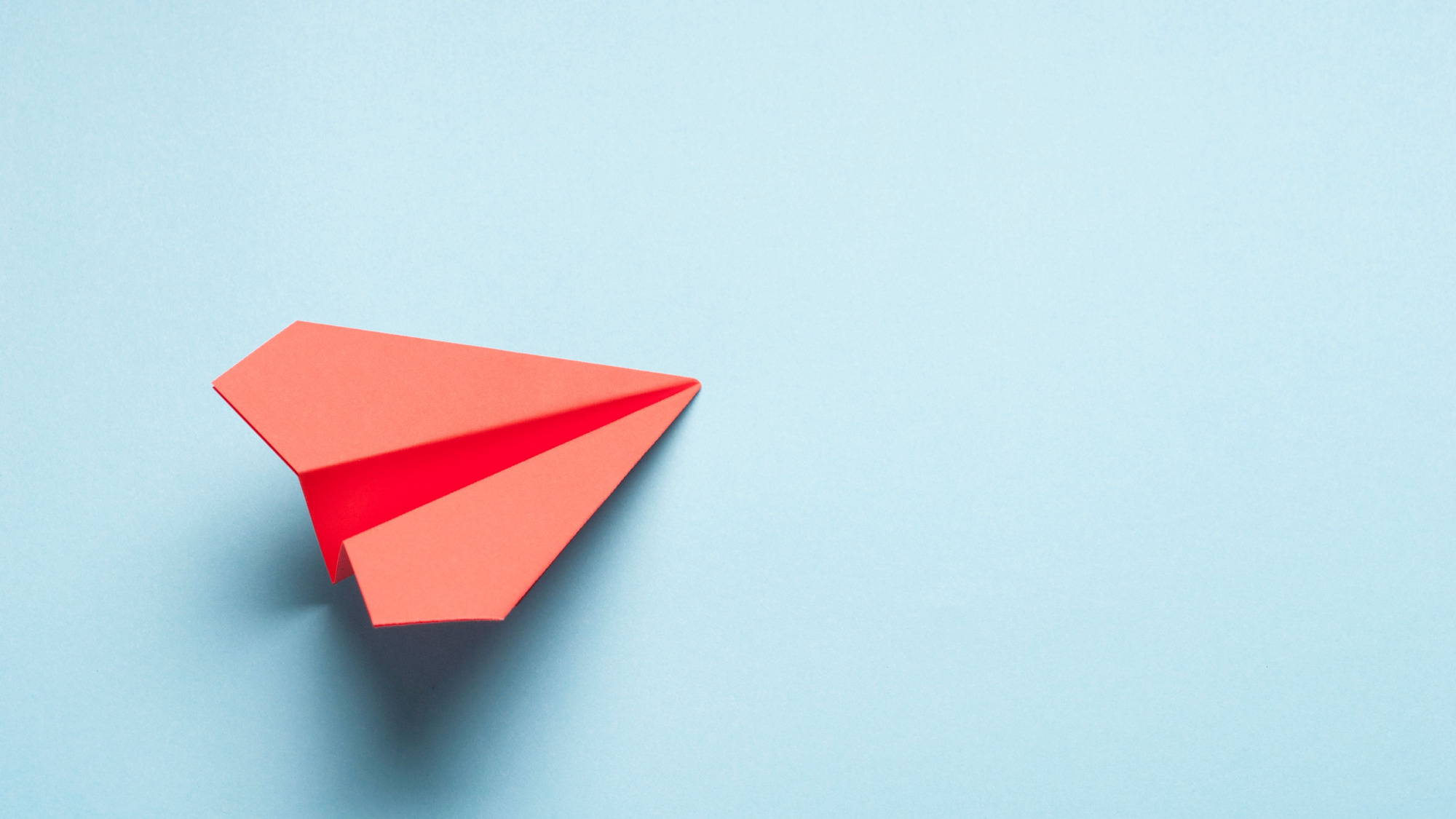 Symbolbild mit rotem Papierflieger vor einem blauem Hintergrund